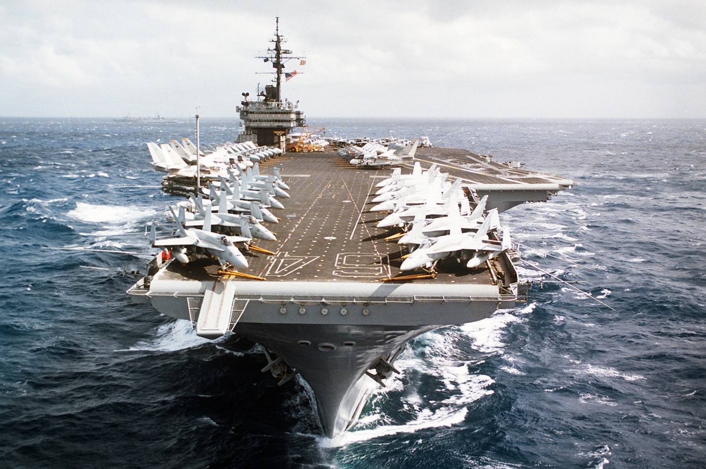 A bow view of the aircraft carrier USS CONSTELLATION (CV-64) underway. Various aircraft of the carrier's air wing are parked on the flight deck - U.S. National Archives & DVIDS Public Domain